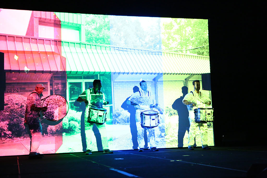 drummers in front of colorful screen with pictures
