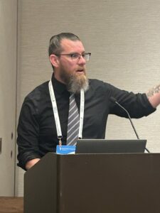 A photo from Building Innovation 2025 shows Nathan Canney at a podium.