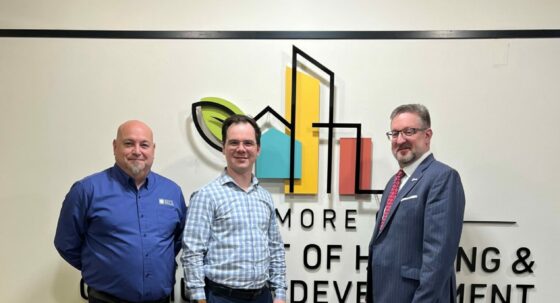 Frank Krech, Mark Howell, and John Boling advocating for facade inspections in front of the Baltimore Dept of Housing & Community Development sign.
