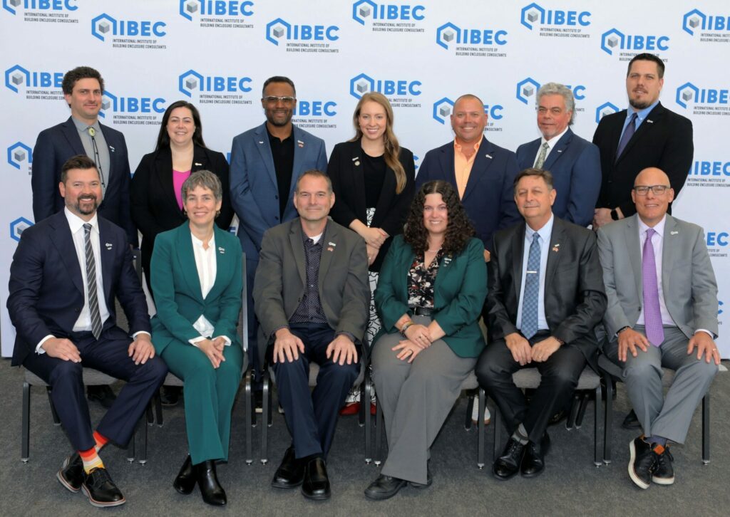 Group of professionals in business attire posing for a group photo at an IIBEC event with a branded backdrop featuring the IIBEC logo.