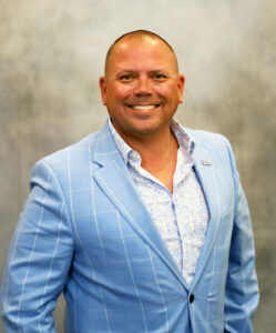 Smiling man in a light blue plaid suit posing for a professional portrait.