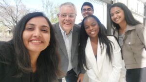 Five friends posing for a selfie outdoors, smiling at the camera with trees in the background.