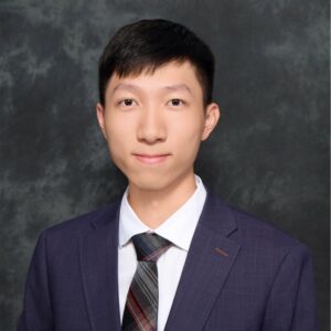 Bright, young man in a dark purple suit and striped tie posing for a formal headshot against a charcoal backdrop.