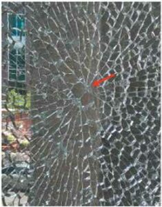 Shattered glass window pane with a spiderweb pattern and an orange arrow pointing to the impact origin.