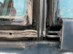 Close-up of a dirty, rusted hinge area with peeling teal paint on heavy equipment.