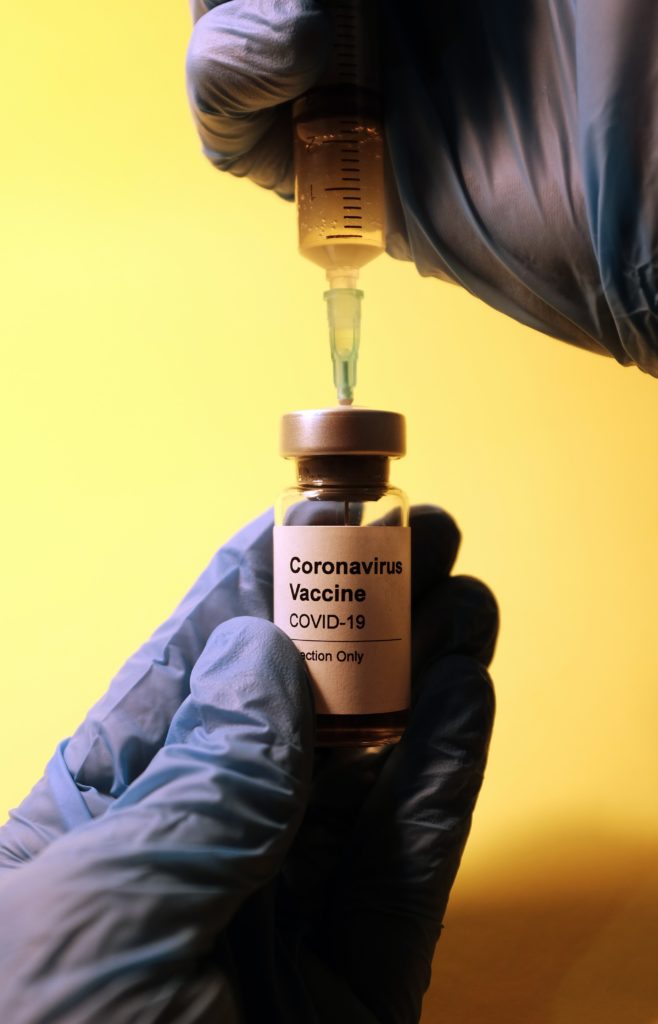 gloved hand holding bottle labeled coronavirus vaccine with syringe